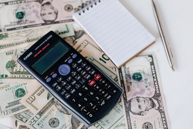 e52bd9e8-26e7-4bdf-953c-0d8394f98d19 a calculator and note pad on top of dollar bills
