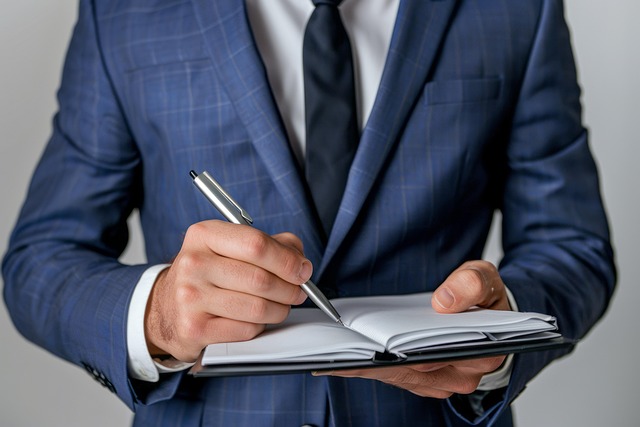 person-in-suit-writing-in-notebook-with-pen