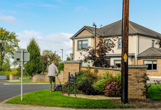 person-mowing-lawn-in-front-of-modern-suburban-house